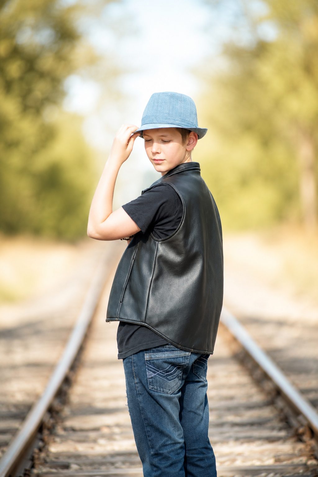 Portrait of a boy in a fedora and leather jacket on a railway line