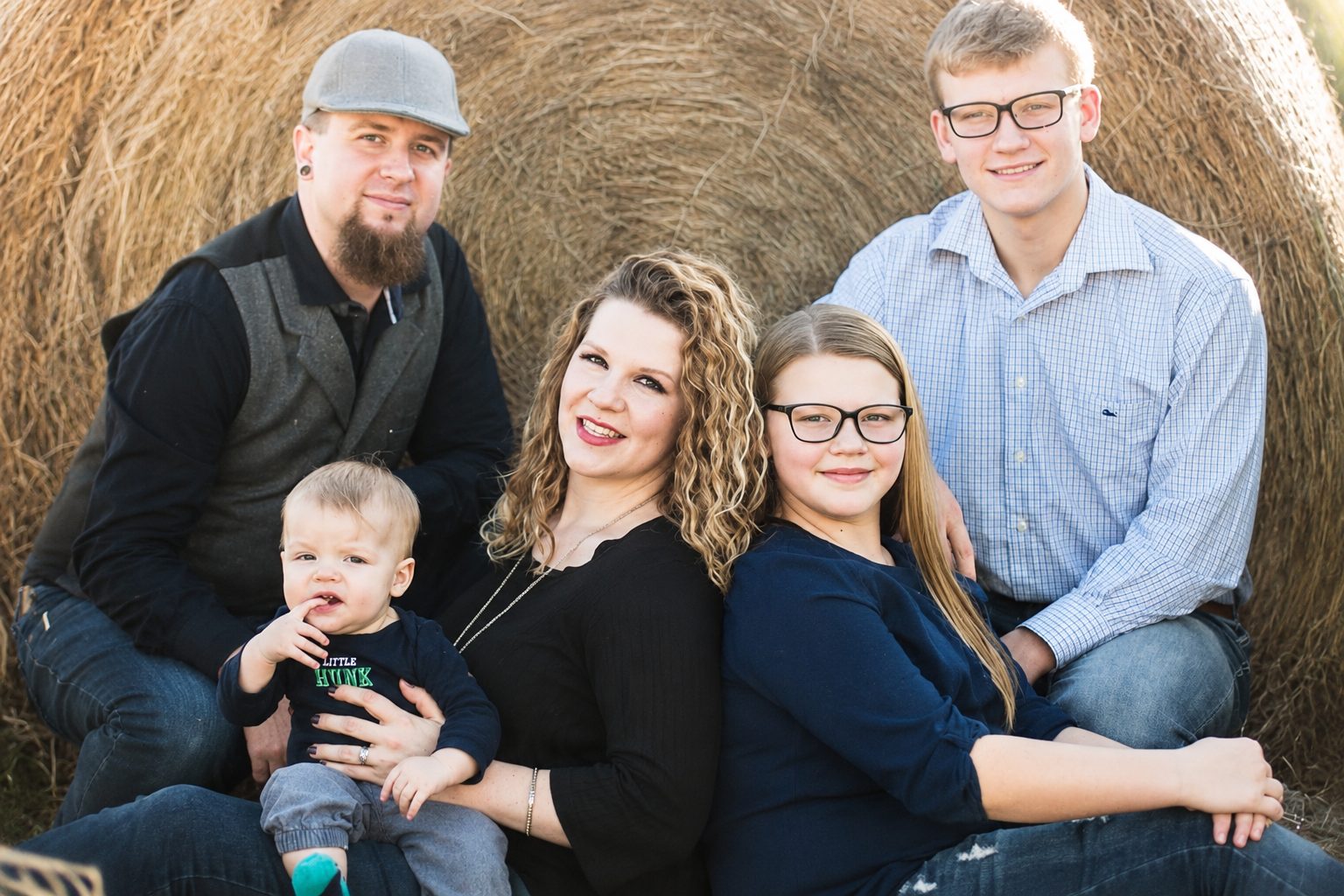 Family of five photographed together against a round hay bale in autumn