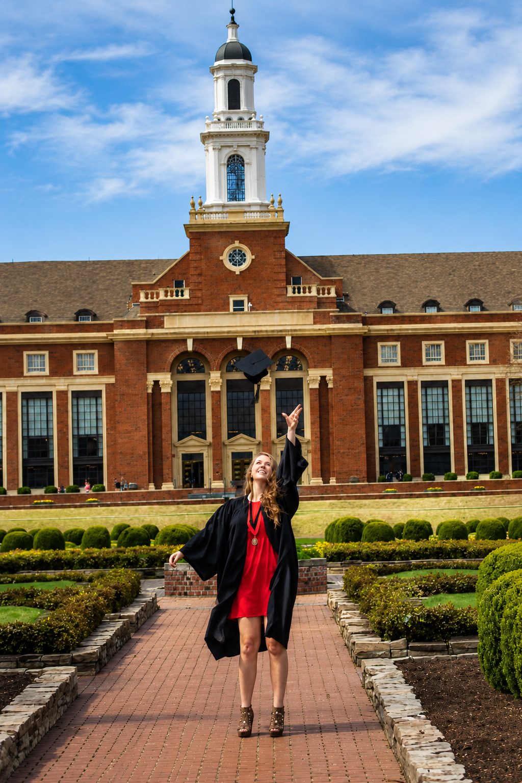 Oklahoma State University graduate in cap and gown celebrating outside the Edmon Low Library in Stillwater