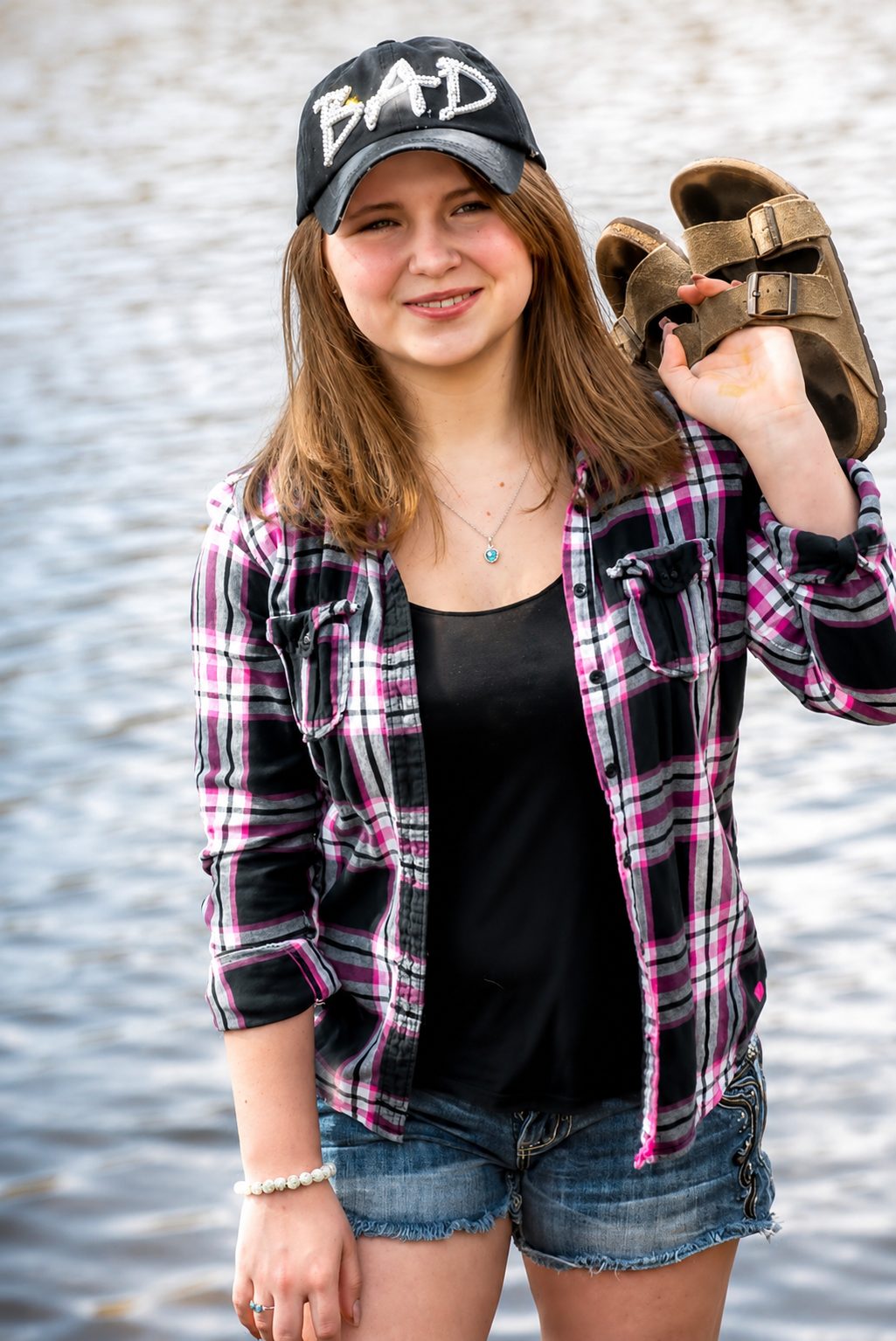 Relaxed senior portrait by the water, boots slung over one shoulder