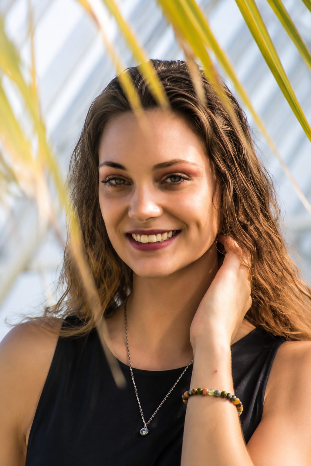Natural light senior portrait of a smiling young woman framed by palm fronds